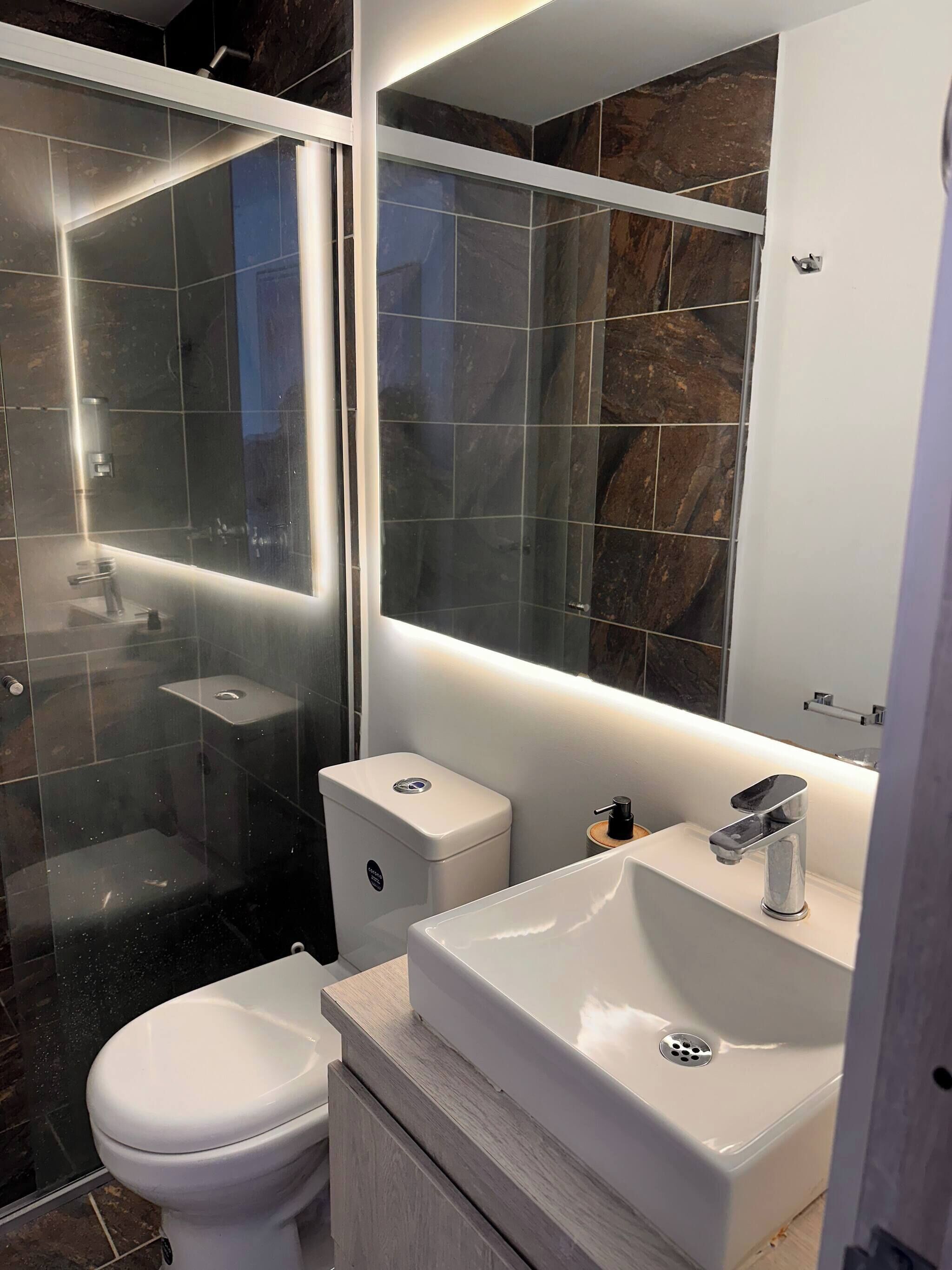 A modern bathroom with a glass-enclosed shower, a white toilet, and a sink with a mirror above.