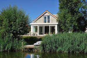 A modern house with a large glass door, a balcony, and a dock extending into a body of water. - Coastal Bungalow with Private Garden (Makkum)
