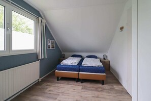 A bedroom with a sloped ceiling, a double bed, a radiator, and a window with curtains. - Waterfront Makkum Bungalow with Jetty (Makkum)