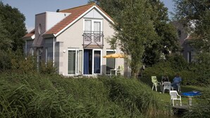 A two-story house with a balcony, a sliding glass door, and a small patio area with chairs and a table. - Waterfront Makkum Bungalow with Jetty (Makkum)