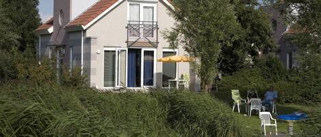 A two-story house with a balcony, a sliding glass door, and a small patio area with chairs and a table.
