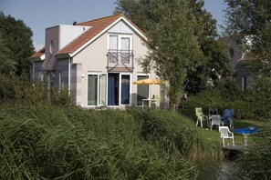A two-story house with a balcony, a sliding glass door, and a small patio area with chairs and a table. - Waterfront Makkum Bungalow with Jetty (Makkum)