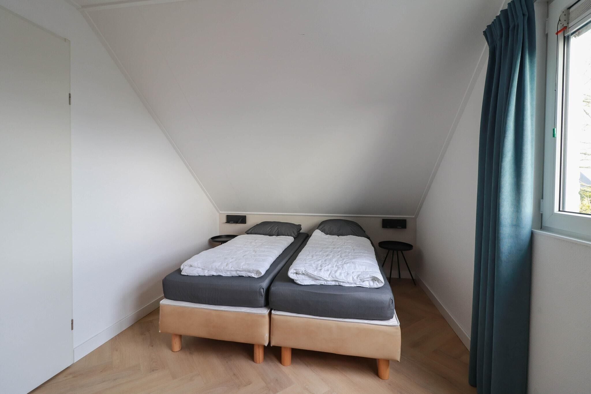 Ein kleines Schlafzimmer mit Schrägwand, zwei Betten, einem kleinen Tisch und einem Fenster mit Vorhängen.