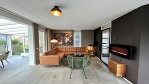 A modern living room with a sectional sofa, a round coffee table, and a flat-screen TV mounted on the wall. - Elegant Waterfront Bungalow for 6 (Makkum)
