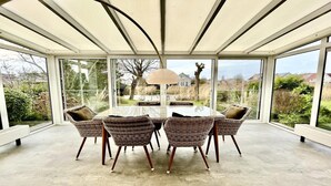 A covered patio with a round table and wicker chairs, large windows, and a view of the outdoors. - Elegant Waterfront Bungalow for 6 (Makkum)