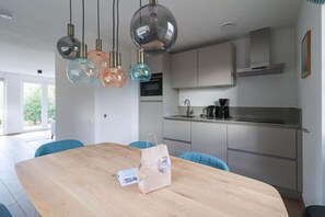 A modern kitchen with a wooden dining table, a coffee maker, and pendant lights. - Elegant Waterfront Bungalow for 6 (Makkum)
