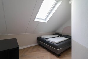 Ein kleines Zimmer mit einem Einzelbett, geneigter Decke und einem Oberlicht.