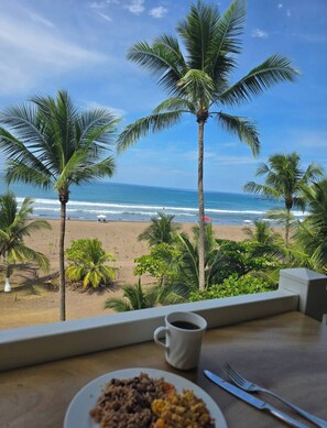 Blick auf einen Strand vom Zimmer aus, mit einem Tisch, einer Speiseplatte und einer Kaffeetasse.