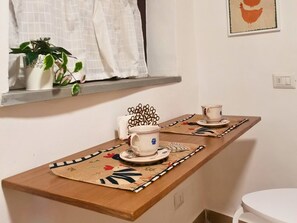 Een keukenhoek met een houten aanrecht, een raam met witte gordijnen, een plant in een pot en een lijst met foto aan de muur.
