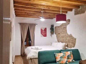 Een slaapkamer met een bed, een groene bank, een plafondventilator, een muur met een stenen textuur, en een poster aan de muur.