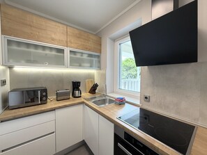 A modern kitchen with a built-in oven, a toaster, a coffee maker, and a window with a view of greenery. - Two Bedroom Sea View Apartment Marisol (Mrljane)