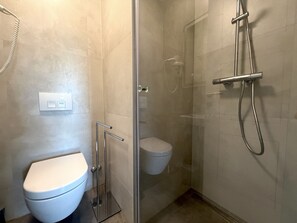 A modern bathroom with a glass-enclosed shower, a toilet, and a wall-mounted light switch. - Two Bedroom Sea View Apartment Marisol (Mrljane)