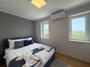A hotel room with a bed, two windows, an air conditioning unit, and a view of the landscape. - Two Bedroom Sea View Apartment Marisol (Mrljane)