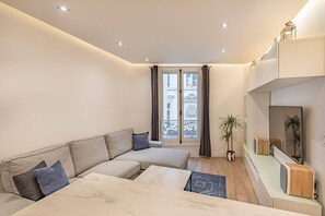 Ein modernes Wohnzimmer mit einem Ecksofa, einem Marmortisch, einer Topfpflanze und einer integrierten TV-Konsole.