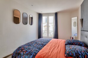 Ein Schlafzimmer mit einem Bett, zwei Spiegeln, einem Fenster mit Vorhängen und einer Tür.