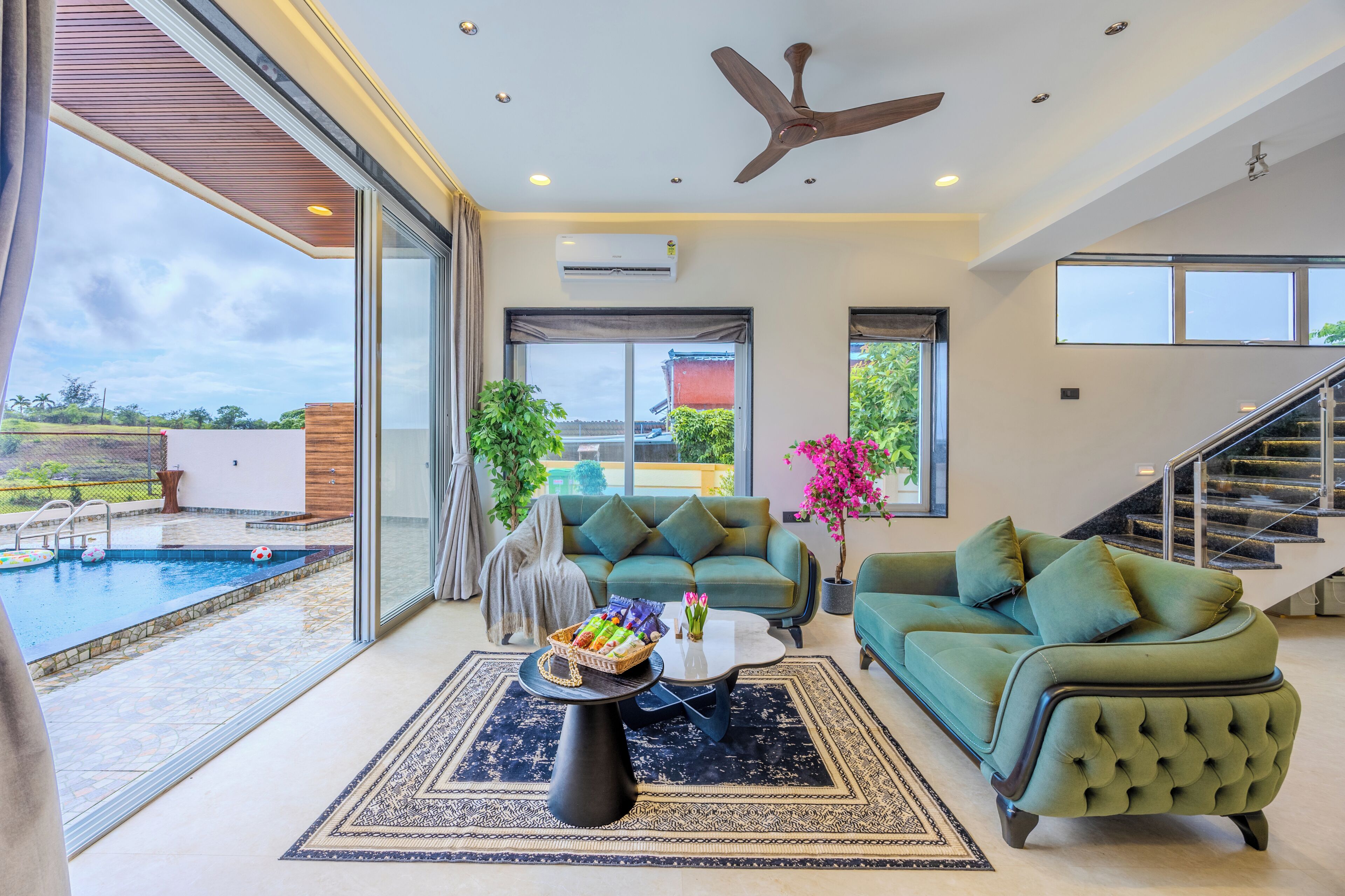 A spacious living area with a pool, green sofas, a coffee table, and a ceiling fan.