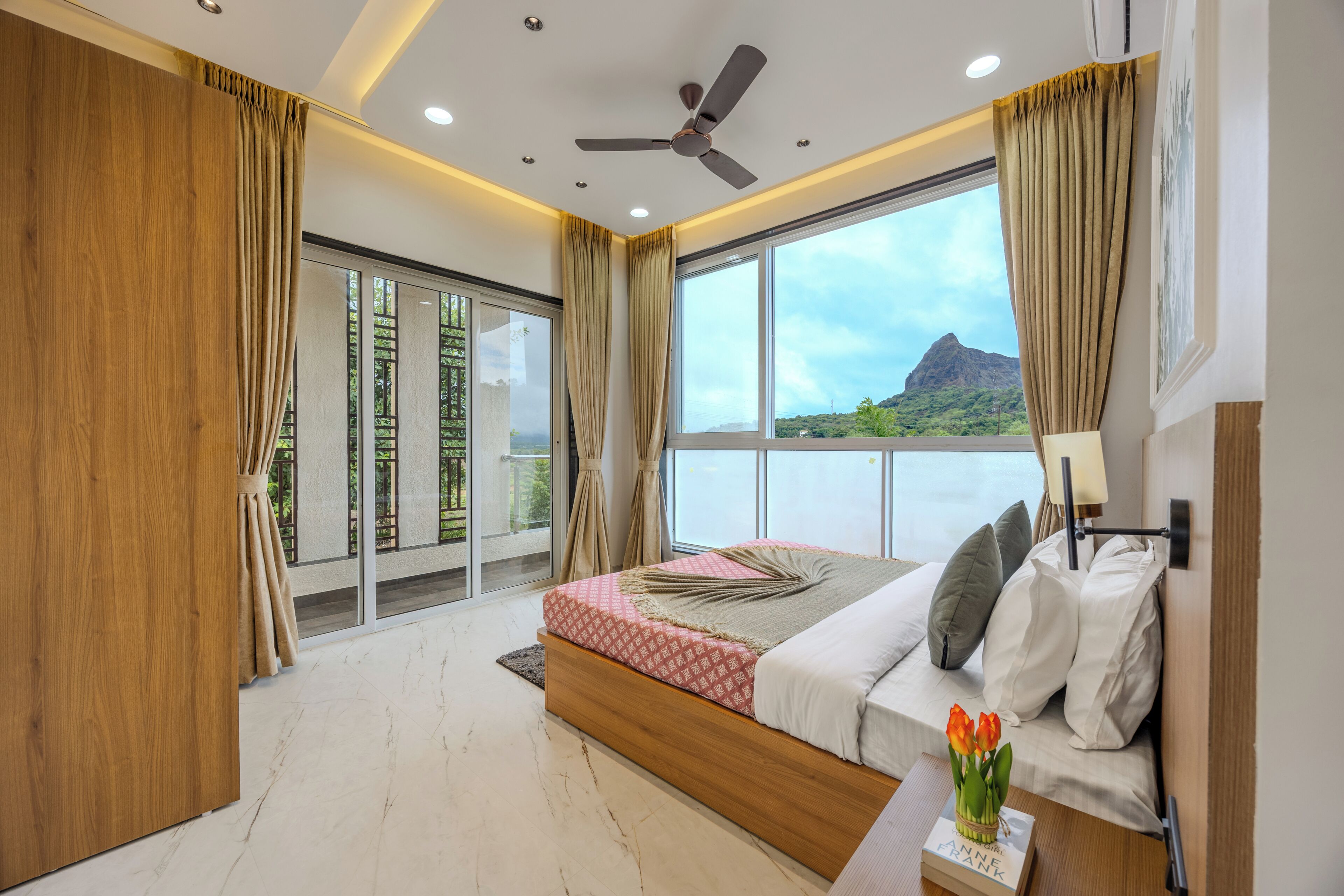 A bedroom with a large window, a bed, a ceiling fan, and a view of a mountain.