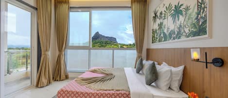 A bedroom with a large bed, a nightstand, a wall-mounted lamp, and a view of the outdoors.