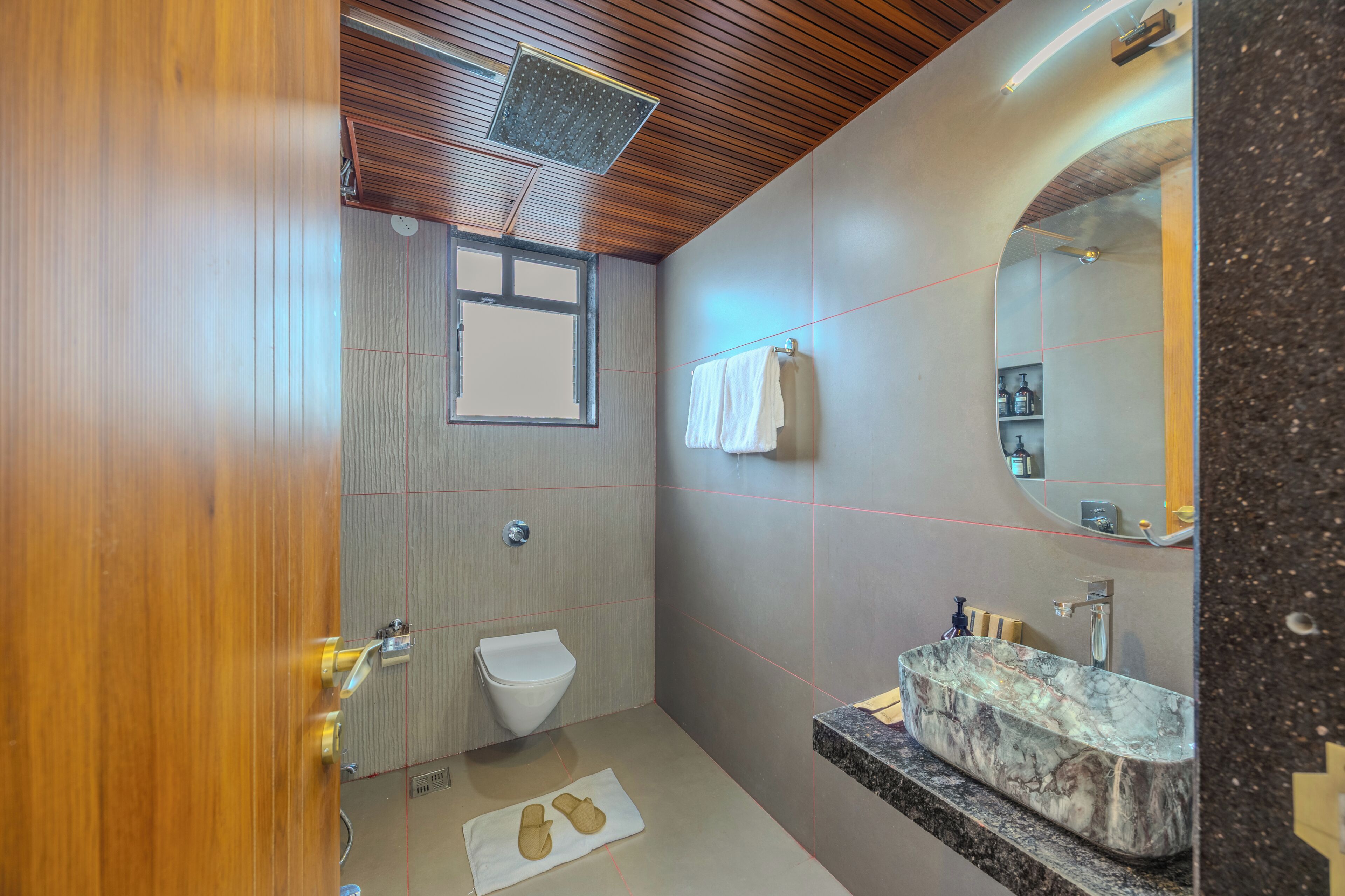 A modern bathroom with a wooden ceiling, a white toilet, a marble sink, and a mirror.