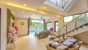A spacious living area with a dining table set for breakfast, a sofa, and a view of a swimming pool. - ELIVAAS RK Villa 4BHK Hideaway with Pool (Lonavala)