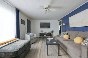 Een woonkamer met een bank, fauteuil, salontafel en een plafondventilator.