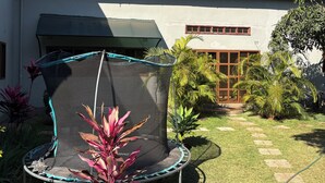Una propiedad residencial con un trampolín en el jardín, rodeada de diversas plantas y una casa con techo verde.