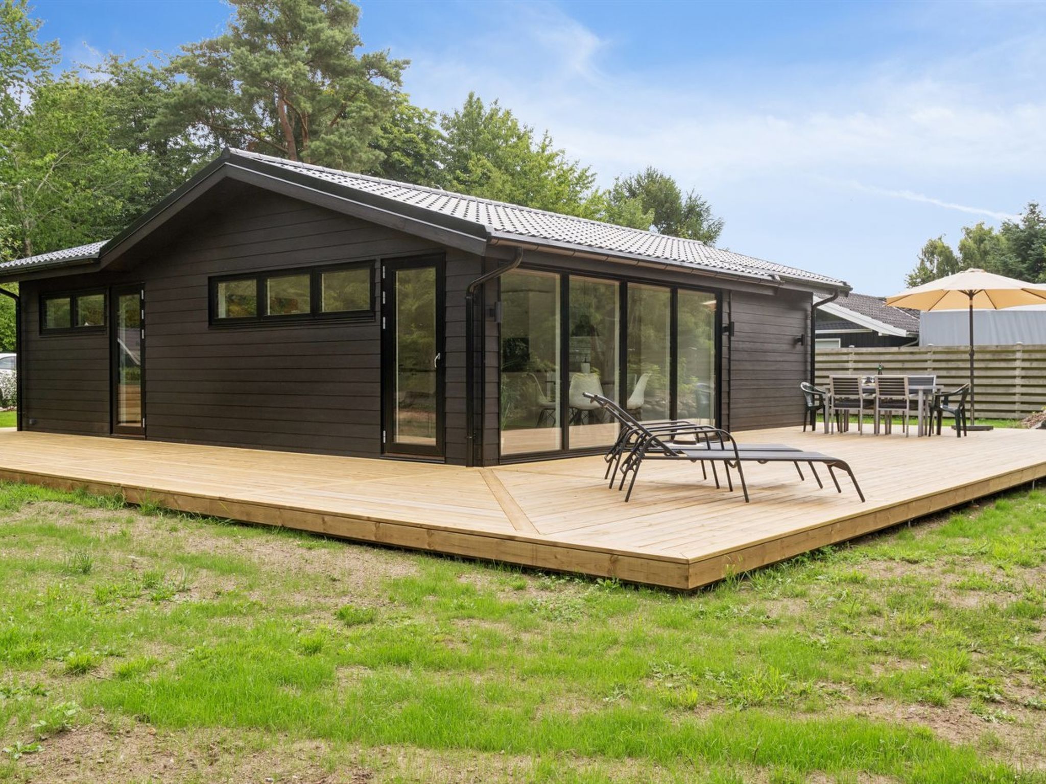 Une maison moderne dotée d’une terrasse, de grandes fenêtres et d’un espace extérieur aménagé et couvert.
