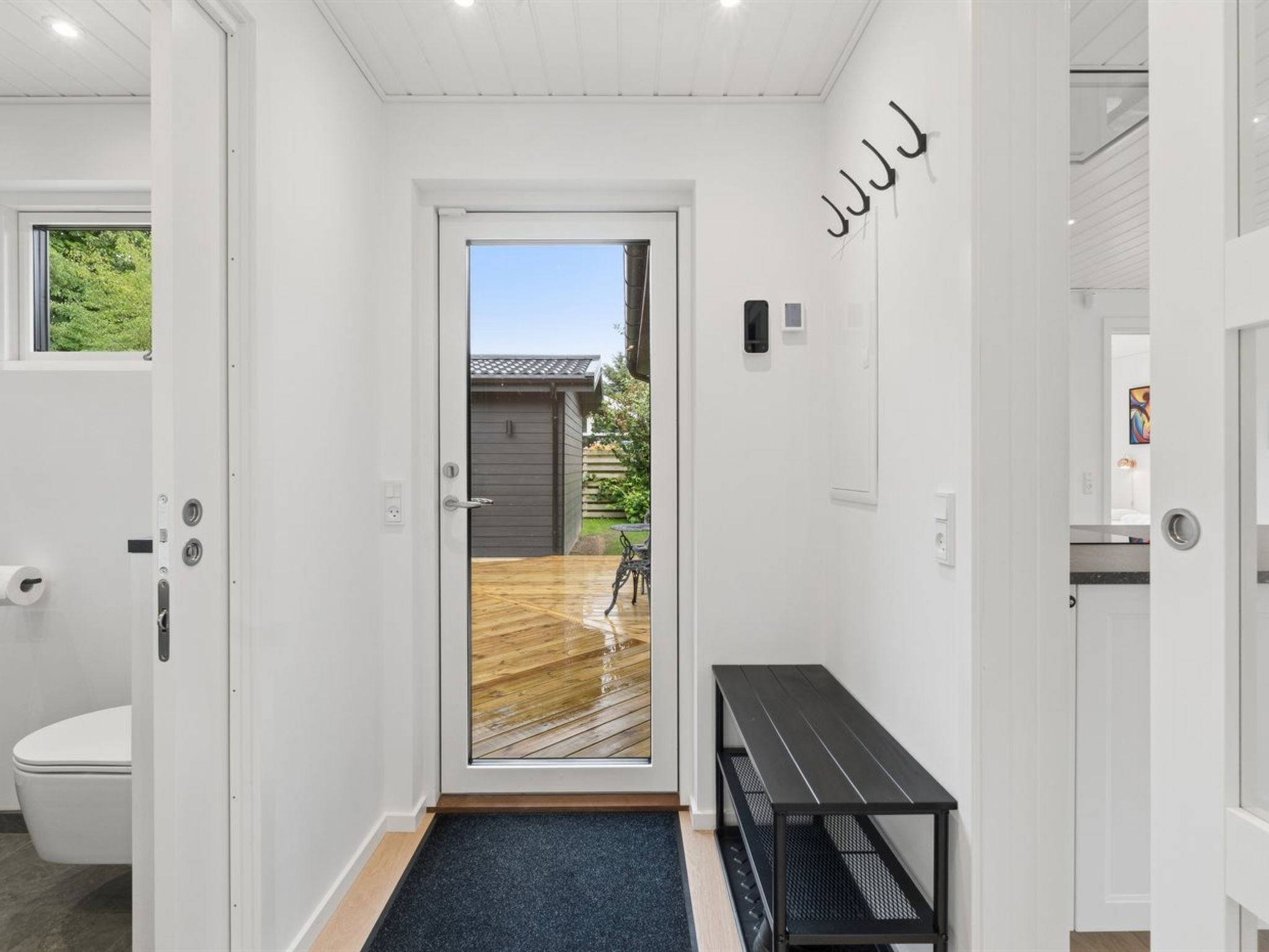 A hallway with a wooden floor leading to a door with a view of a backyard.