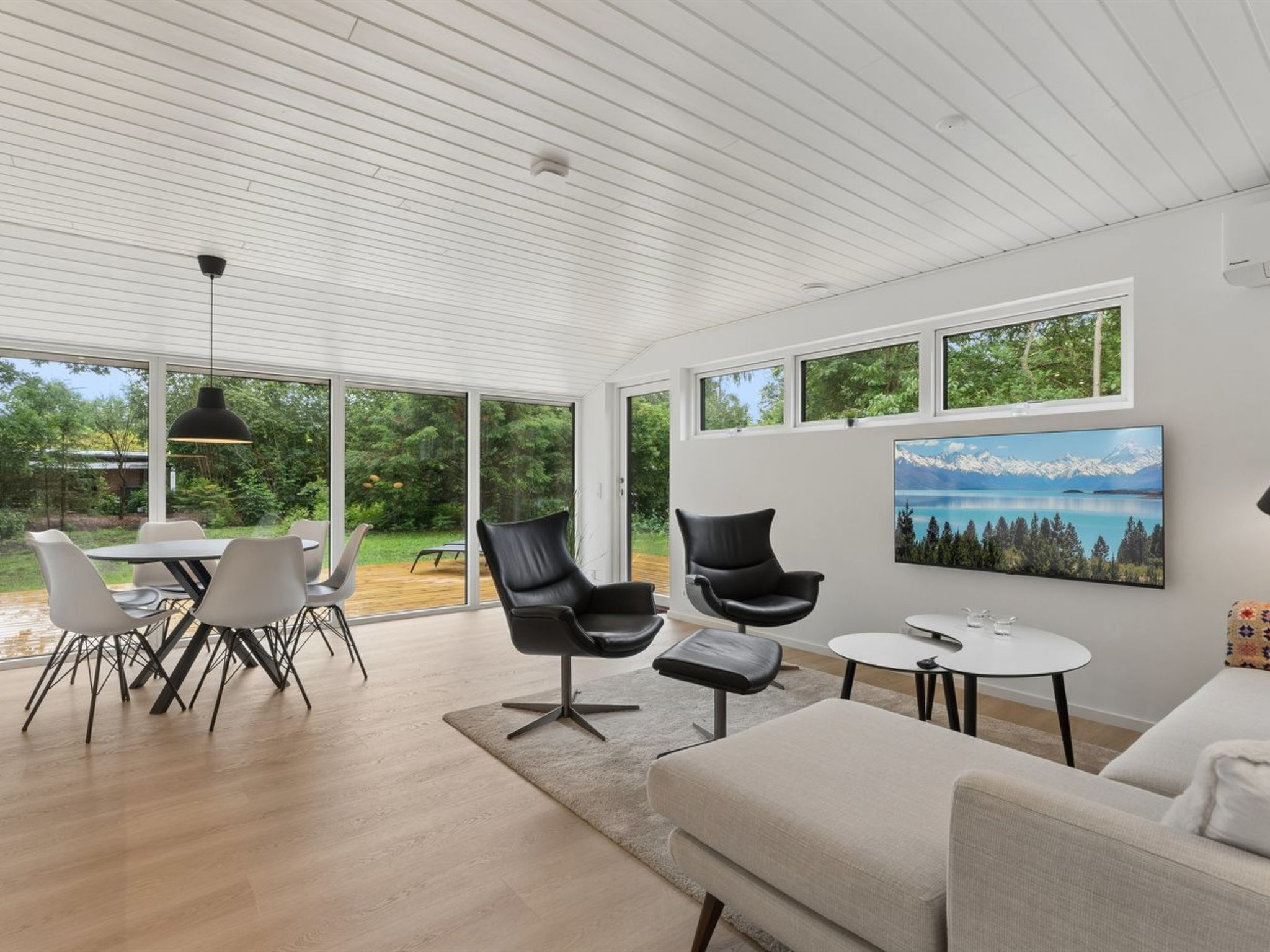Una sala moderna con comedor, ventanas amplias y un cuadro de un paisaje montañoso.