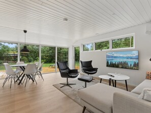 Ein modernes Wohnzimmer mit Essbereich, großen Fenstern und einem Gemälde einer Berglandschaft.