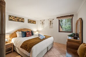 A bedroom with a large bed, a nightstand, a dresser, and a window with a view of trees. - River’esque | Spa Bath | Forest Views (Margaret River)