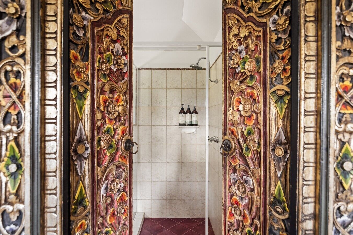 A bathroom with ornate doors, a shower, and a shelf with toiletries.