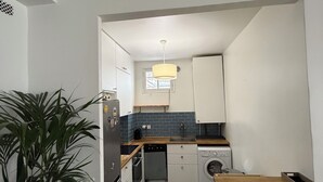 Uma cozinha com armários brancos, lava-louças, máquina de lavar roupa e um vaso de planta.