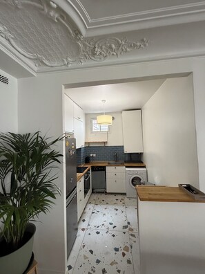 Eine Küche mit weißen Schränken, einem Geschirrspüler, einer Waschmaschine und einem Blumentopf.