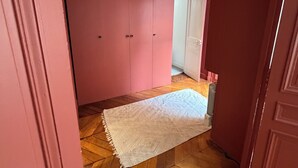 Um corredor com piso de madeira, um tapete branco e paredes cor de rosa.