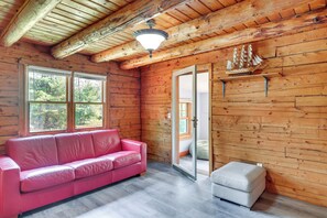 A cabin interior with a wooden ceiling, a pink leather sofa, a white ottoman, and a ship model on the wall. - Classic New England Cabin on Belleau Lake (East Wakefield)