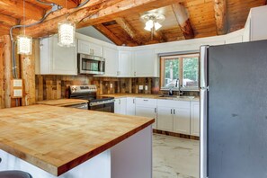 A kitchen with wooden beams, white cabinets, a stainless steel refrigerator, and a wooden countertop. - Classic New England Cabin on Belleau Lake (East Wakefield)