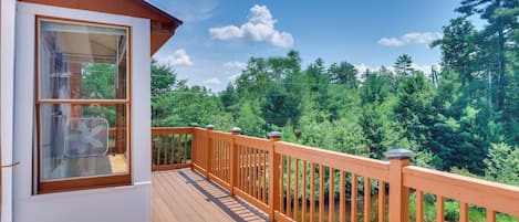 A wooden deck with a railing, a window with a fan, and a view of a forest.