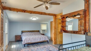 Ein Schlafzimmer mit einem Bett, einem Nachttisch, einem Deckenventilator, einem Fenster mit Jalousien und einer Holztür.