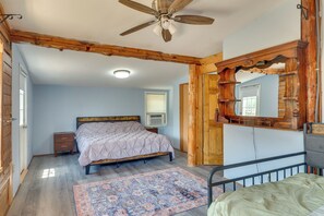 Ein Schlafzimmer mit einem Bett, einem Nachttisch, einem Deckenventilator, einem Fenster mit Jalousien und einer Holztür.