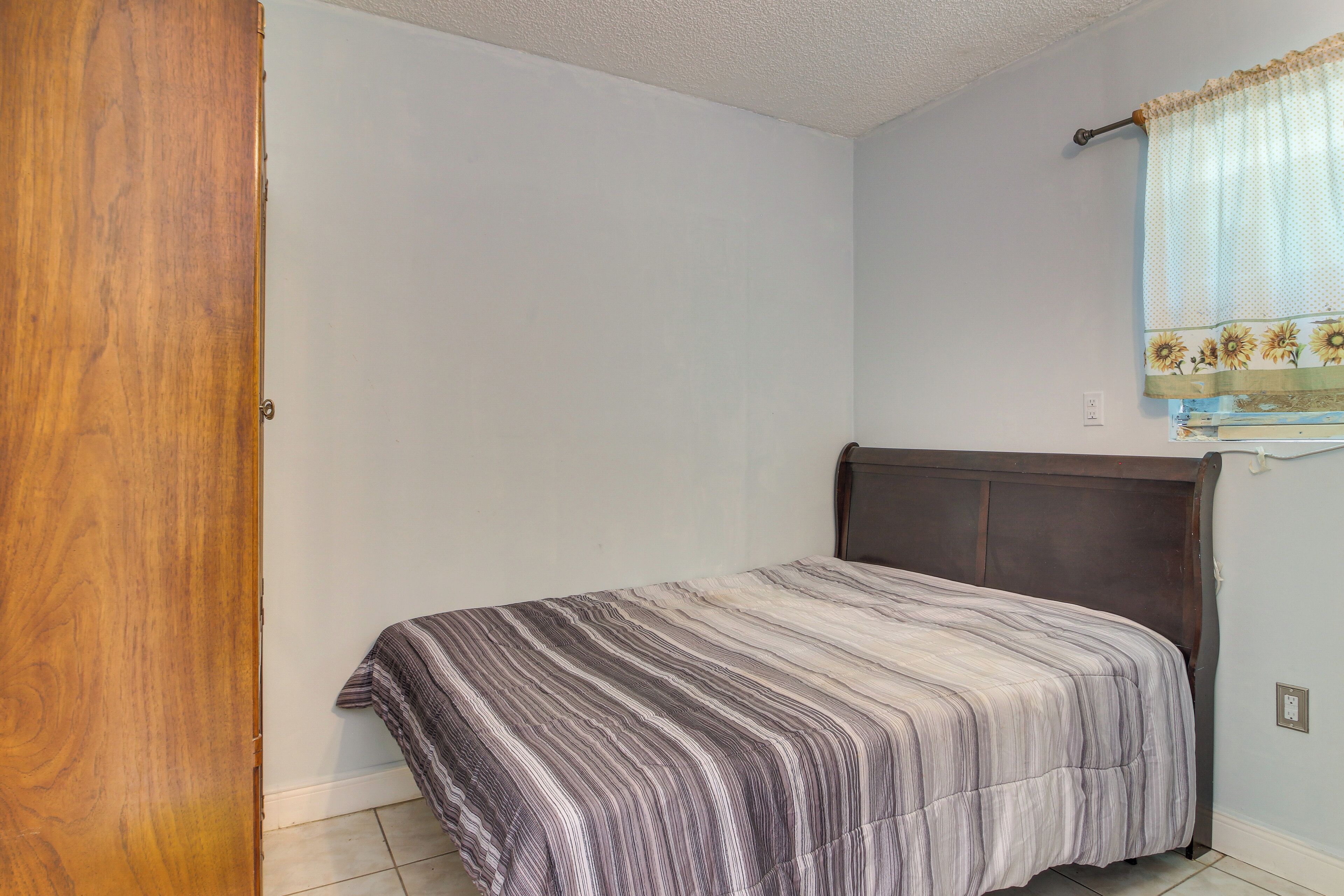 Un dormitorio con cama, puerta de madera y ventana con cortina.