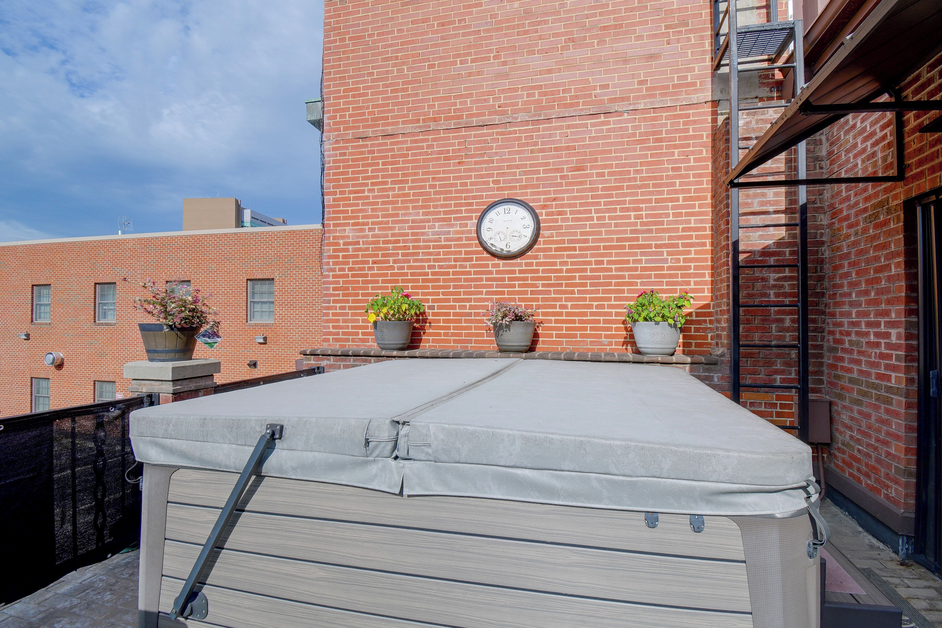 Une terrasse sur le toit, avec un mur en briques, une horloge et des plantes en pot.