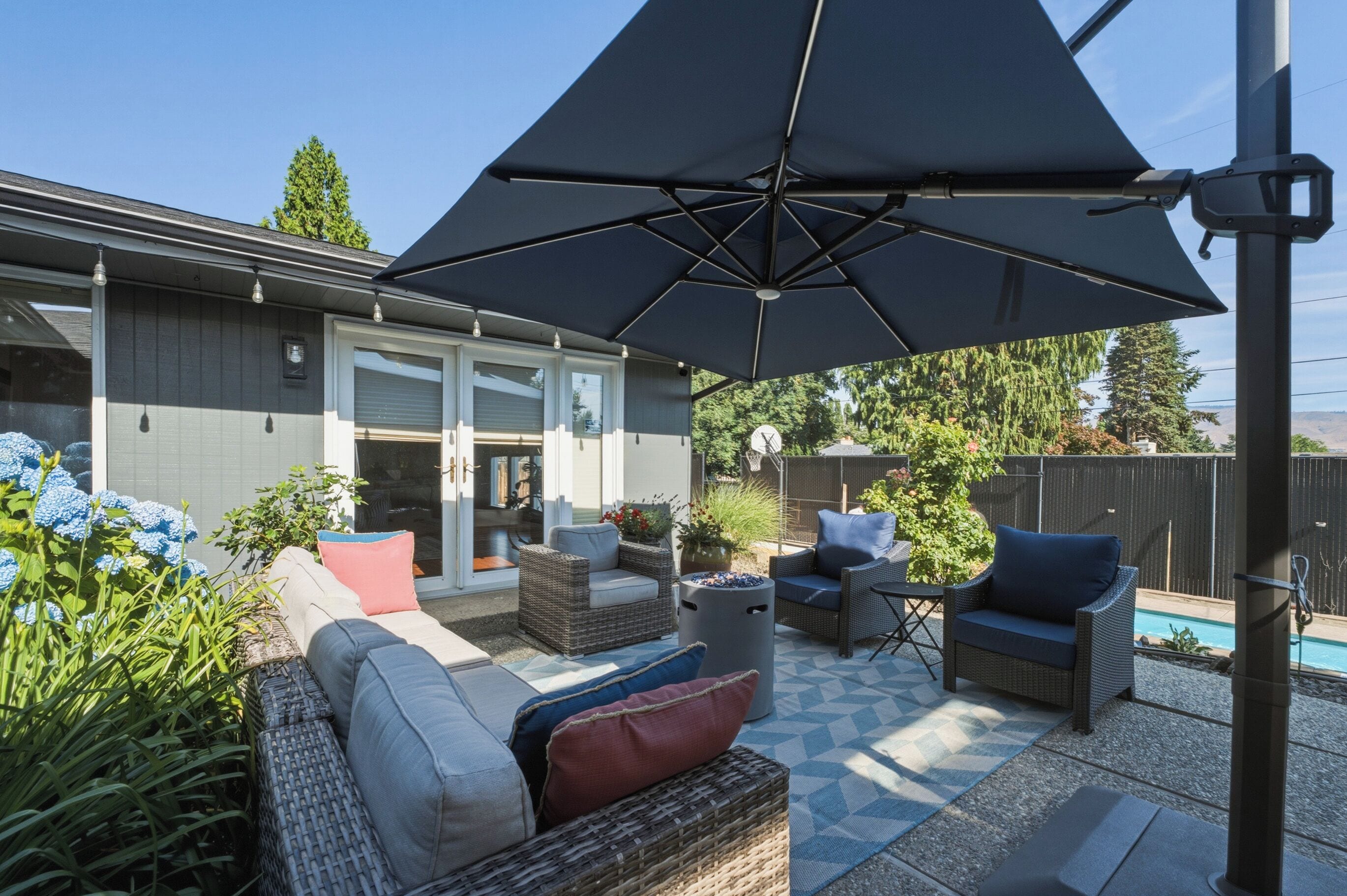 Un patio con mobiliario exterior, un parasol grande y una piscina al fondo.