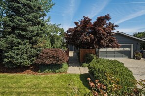 Una propiedad residencial con un césped cuidado, un gran árbol de coníferas y un garaje.