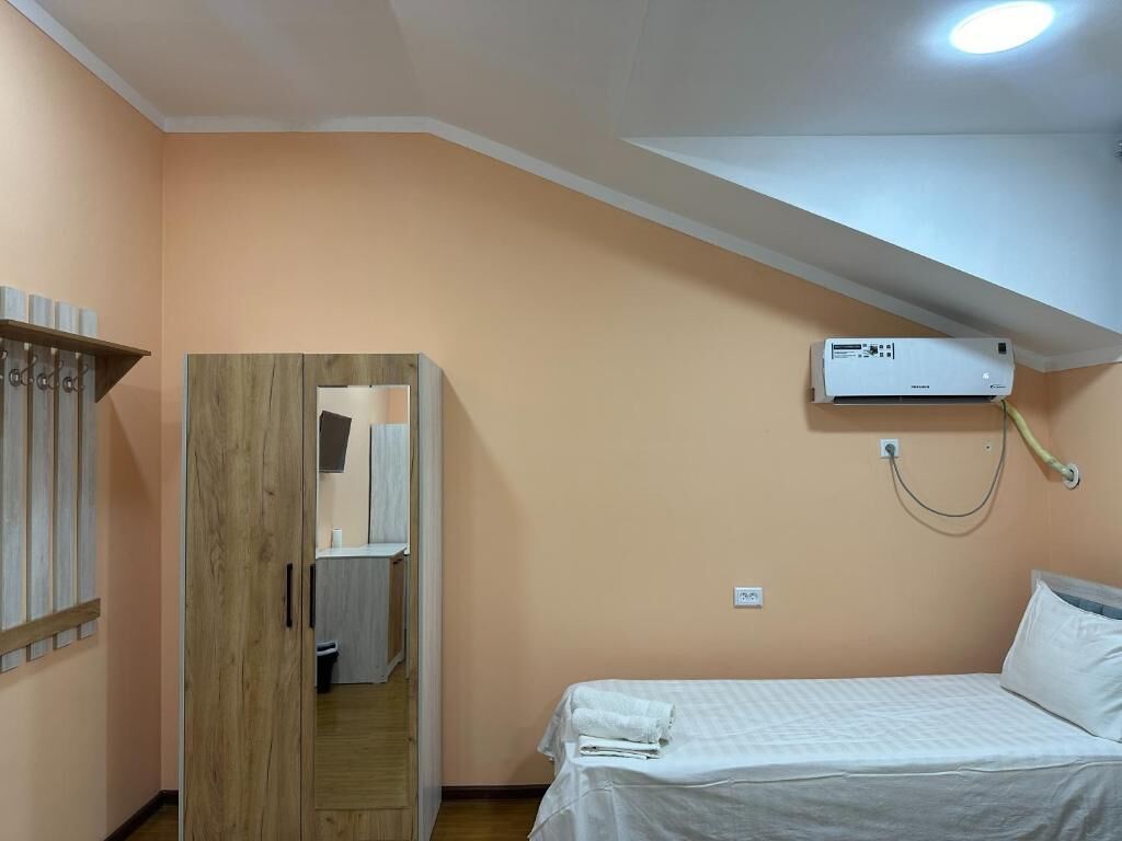 A bedroom with a bed, an air conditioning unit, a wooden wardrobe, and a small bathroom.