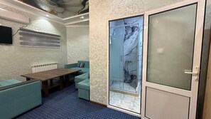 A room with a wooden table, teal armchairs, a glass door with a marble pattern, and a white radiator.