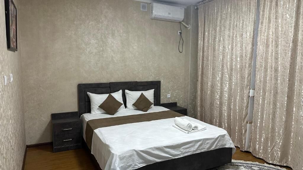 A bedroom with a bed, a nightstand, a wall-mounted air conditioner, and a curtain.