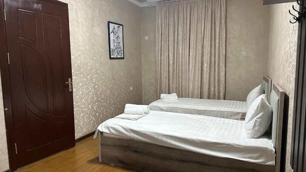 Ein Zimmer mit zwei Betten, einer Holztür, einem gerahmten Bild an der Wand und einem Vorhang.