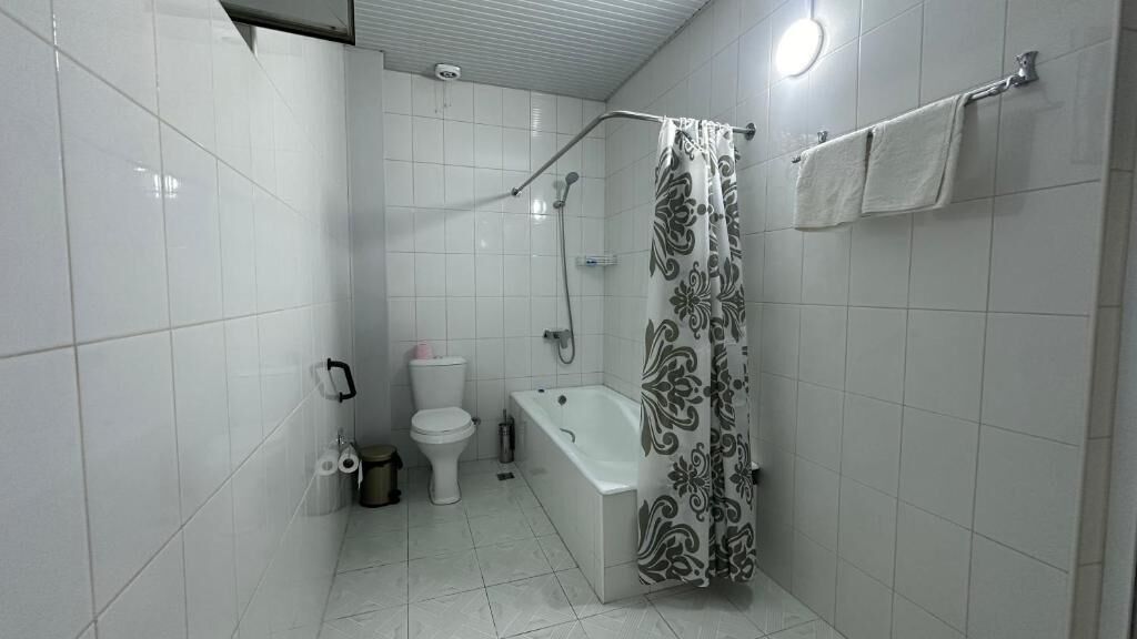 A bathroom with white tiles, a toilet, a bathtub, and a shower curtain.