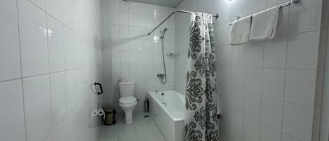 A bathroom with white tiles, a toilet, a bathtub, and a shower curtain.